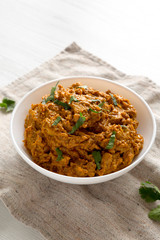 Homemade Chicken Tikka Masala in a white bowl on a white wooden background, low angle view.