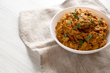 Homemade Chicken Tikka Masala in a white bowl on a white wooden surface, side view. Copy space.