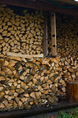 Logs of firewood piled under the roof of slate. Fuel for stove heating. Country life. Wooden firewood stacked wall. Natural wood background. Firewood stacked in several rows