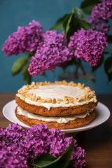 Carrot cake with hazel nuts and bouquet of purple lilac on the wooden table