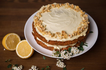 Obraz na płótnie Canvas Carrot cake with hazel nuts, white flowers of meadowsweet and slice lemon on the wooden table