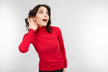 brunette girl in a red sweater overhears a conversation on a white studio background