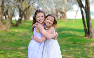 Beautiful young girls with blue eyes in a white dresses in the garden with apple trees blosoming having fun and enjoying smell of flowering spring garden.