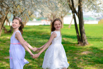 Fototapeta na wymiar Beautiful young girls with blue eyes in a white dresses in the garden with apple trees blosoming having fun and enjoying smell of flowering spring garden.