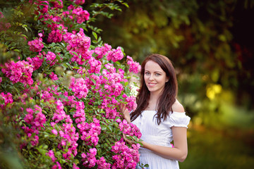 portrait of a happy, cute brunette 30-33 years old in a summer park near a rose bush