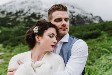 Beautiful bride and groom hug and kiss in the mountains.