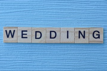 gray word wedding in small square wooden letters with black font on a blue background