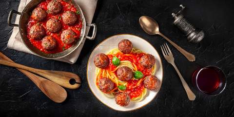 Meatballs with tomato sauce and spaghetti panorama, overhead shot on a dark background