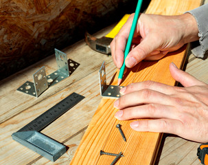 Carpenter tries on a furniture corner using a pencil. Makes a mark before screwing the corner to the wooden Board.