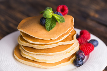 Pile of pancakes with blueberries and raspberries for breakfast on wooden table.