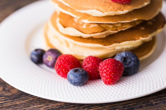 Pile of pancakes with blueberries and raspberries for breakfast on wooden table.