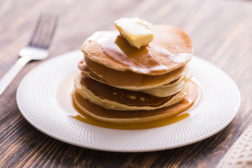 Small pancakes with maple syrup and butter on wooden table. Breakfast concept.
