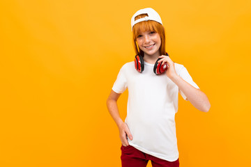 smiling european red-haired girl in a white t-shirt with headphones on a yellow background.