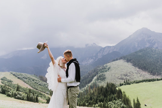 Beautiful bride in a boho style dress and groom hug and kiss on a field near the mountains. Wedding photo shoot in the mountains. Black and white photo of a bride and groom in the mountains.