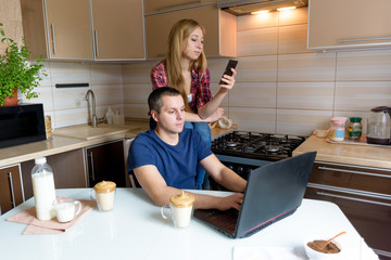 a man and a woman with a laptop communicate online, sitting in the kitchen with dalgona coffee . freelance at home. concept of social distance, work at home, online communication, virtual friends