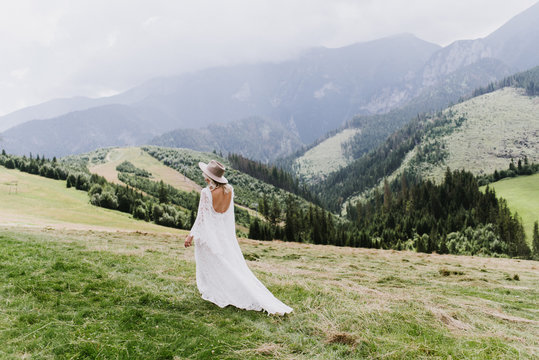 Beautiful bride in a dress in the style of boho walks on the field against the backdrop of the mountains. Wedding photo shoot in the mountains.