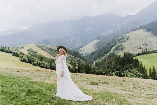 Beautiful bride in a dress in the style of boho walks on the field against the backdrop of the mountains. Wedding photo shoot in the mountains.