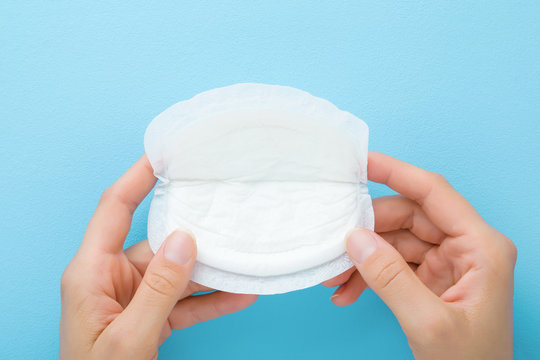 Young mother hand holding white breast pad on light blue table background. Pastel color. Bra and clothes protection in breastfeeding time. Closeup. Point of view shot. Top down view.