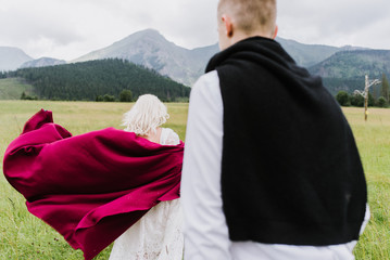 Beautiful bride in a boho style dress and groom walk on the field near the mountains. Wedding photo shoot in the mountains.