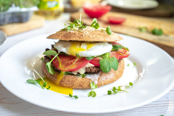 Homemade beef cheese burger with whole grain buns, poached egg, tomatoes and microgreens close up, healthy food