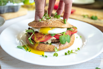 Person hold healthy homemade beef cheese burger with whole grain buns, poached egg, tomatoes and microgreens, healthy food