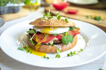Healthy homemade cheeseburger with whole grain buns, beef cutlet, poached egg, tomatoes and microgreens
