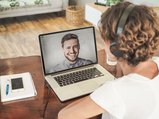 Fototapeta na wymiar woman having a video conference call with a man on her laptop wearing a headset with notepad and mobile phone on the desk in her home office