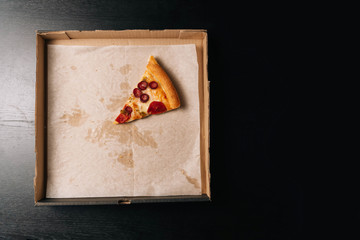 Closeup of the last whole slice of pepperoni pizza in a cardboard paper box on a dark background. View from above