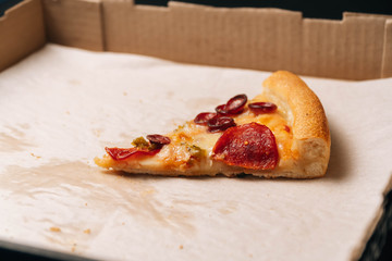Closeup of the last whole slice of pepperoni pizza in a cardboard paper box on a dark background