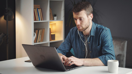 Dutiful young man using laptop sitting at desk working or studying from home during virus pandemic