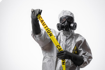 A man in a protective suit and gas mask holds a yellow tape 