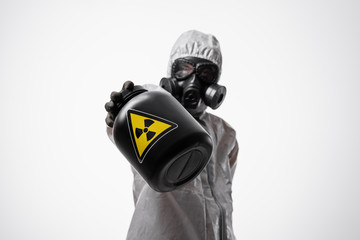 A scientist man in a protective radiation suit and gas mask holds a large black jar  with...