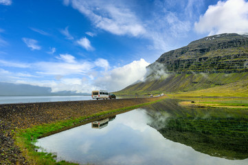 Obraz premium Sedans and sleeper trailers run on the highway. Both sides are lakes. Stagnant water such as mirrors reflecting mountains and blue skies. In Iceland, tourists like to rent a car to drive and travel.