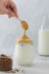 Dalgona Coffee, a trendy fluffy creamy whipped coffee. Making a cool fluffy whipped coffee. Frothy Latte espresso with coffee foam in glass with milk bottle on background.