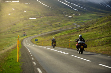 Two motorcycles running on the hill road Head to the great mountain and there is a winding road. In the summer season, bikers like to drive for group trips in Iceland.