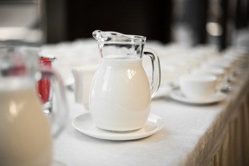 Carafe of milk on the white plate on a table. Catering table. 
