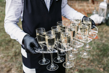Waiter serving champagne. Black gloves and uniform. 
Outdoor area