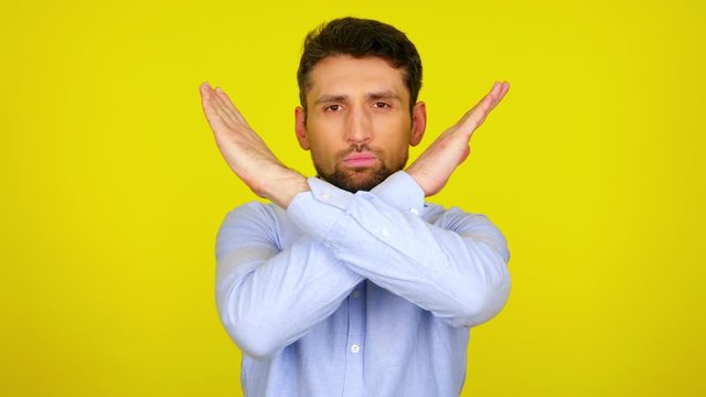 Stop concept: virus, violence, abortion, corruption, inequality, plastic, racism. Serious bearded man in a light blue shirt crossed his arms in front of his chest on yellow background with copy space
