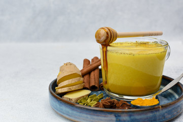 Golden milk or turmeric latte with curcuma powder on light background copy space. Healthy ayurvedic drink. Trendy Indian natural detox beverage with spices for vegans