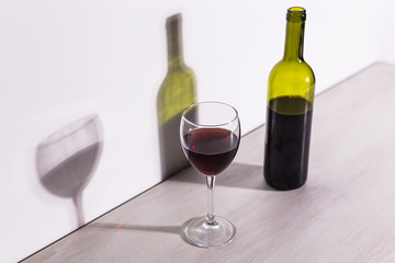 A glass of wine and a bottle casts a long shadow from the evening sun.