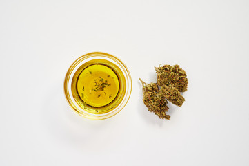marijuana buds and a small bowl of cbd oil on a white background