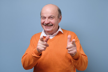 Handsome mature man in orange sweater pointing at camera at you. You are excellent guy. Studio shot