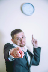 You're late! Angry handsome businessman wearing suit pointing at You and at clock suggesting you are late for work. Job, responsibility, success, timemanagement concept. Selective focus.