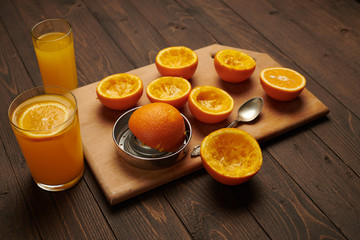Fresh orange fruits whole and squeezed on a wooden table, cutting board - natural and healthy food. Glass of fruit cocktail.