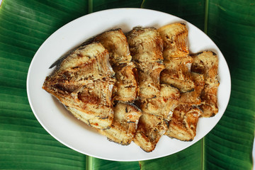 Chunks of crispy leaf fish on white plate on green banana leaf