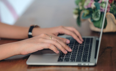 Cropped shot of woman hands typing on laptop keyboard while sitting at wooden table.