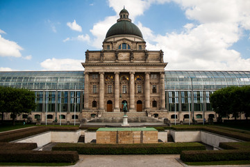 Obraz premium Hoftgarten: Front view of the State chancellery in the city center of the Bavarian capital with Duke of Bavaria statue, war memorial and green sunny park.