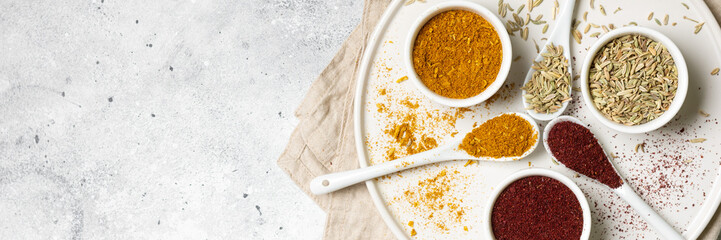 Spices and condiments in white cups and spoons on a light gray table.Fennel, sumac, Curry in white masks. Spices close-up with space for text. The view from the top. Banner.