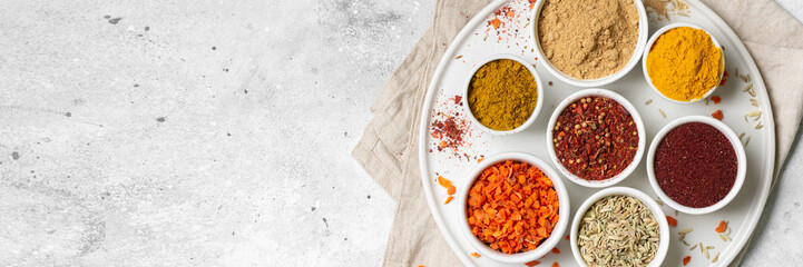 Spices and condiments in white cups and spoons on a light gray table.Fennel, sumac, Curry in white masks. Spices close-up with space for text. The view from the top. Banner