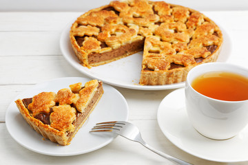 Homemade pie with cottage cheese and prunes and cup of tea on white wooden table. Shallow focus.